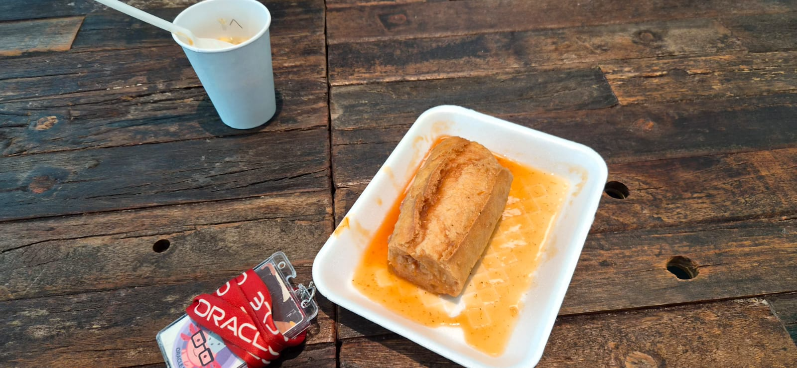 A burrito on a plate with sauce beside a drink on a wooden table.